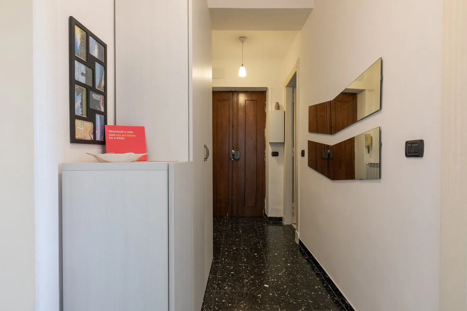 Un pasillo estrecho con suelo oscuro, puerta de madera y espejos en la pared.