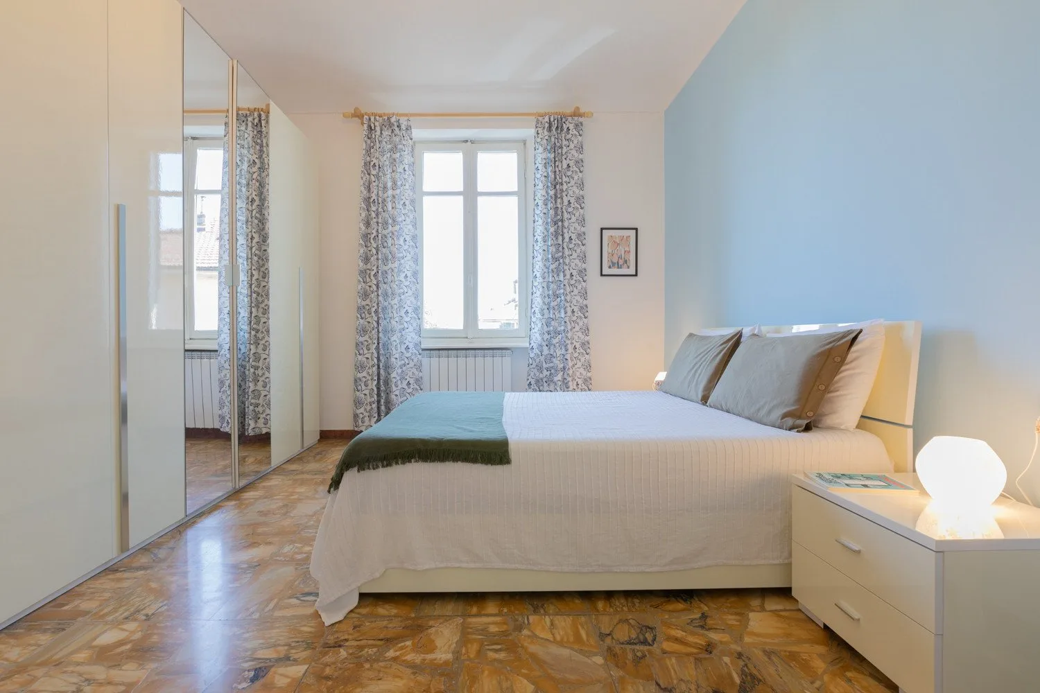 Un dormitorio luminoso con una cama bien tendida y una ventana enmarcada por cortinas.