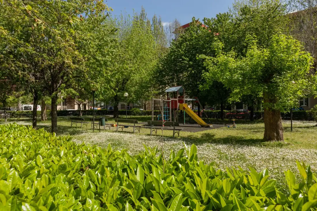Un parque infantil frondoso con una pequeña estructura de juegos y tobogán entre los árboles.