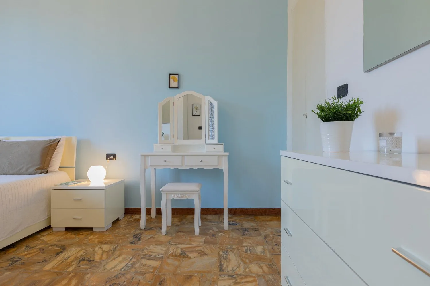 Un dormitorio con tocador blanco y mesita de noche junto a paredes azul claro.
