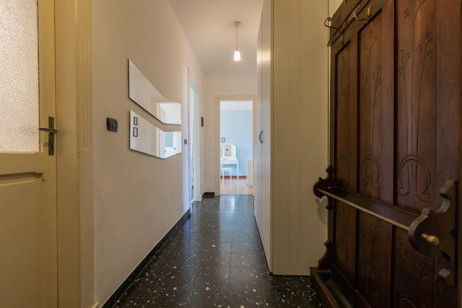 Un pasillo estrecho conduce a una habitación luminosa, con una puerta de madera oscura en primer plano.