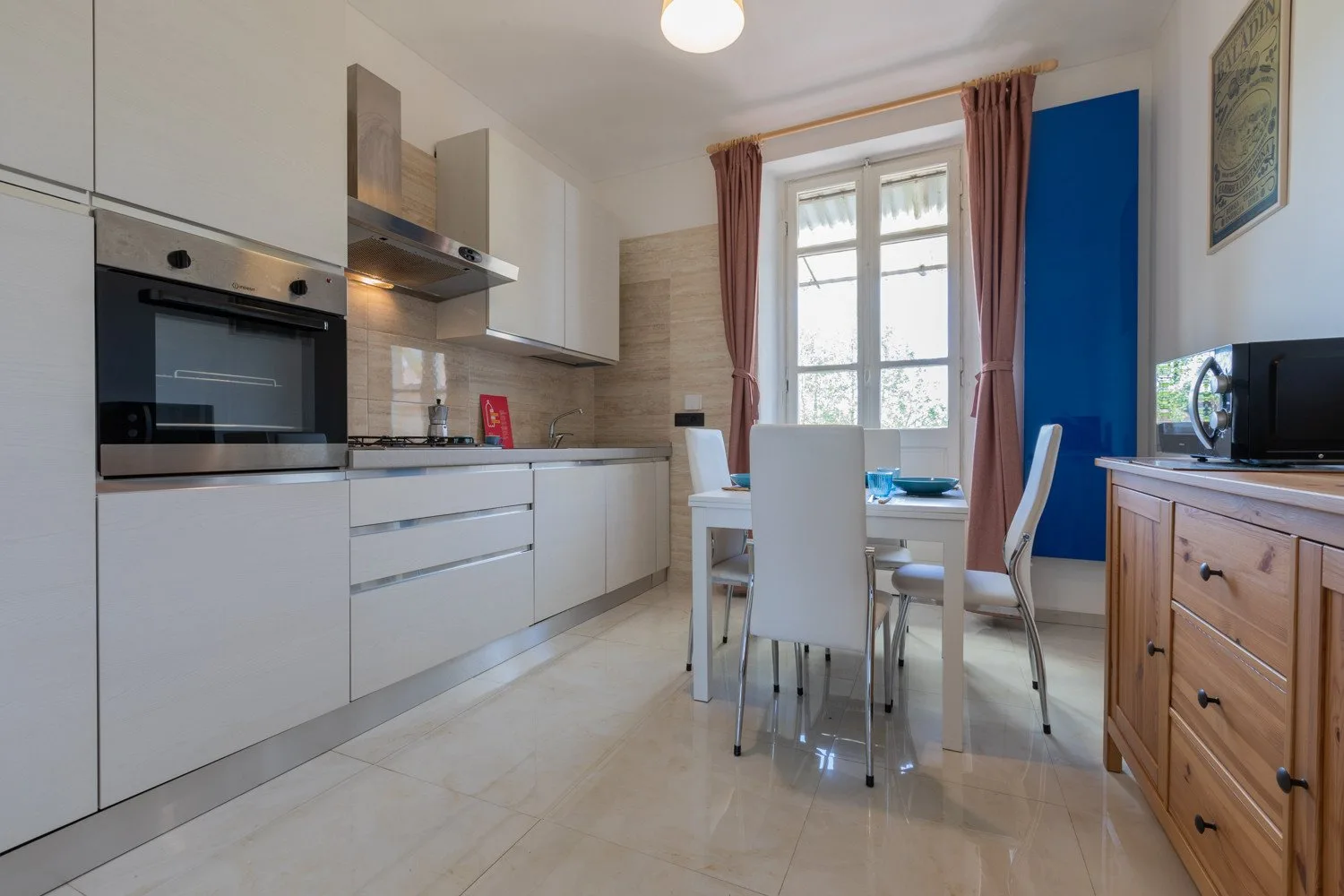 Una cocina-comedor luminosa con armarios blancos y una mesa junto a la ventana.