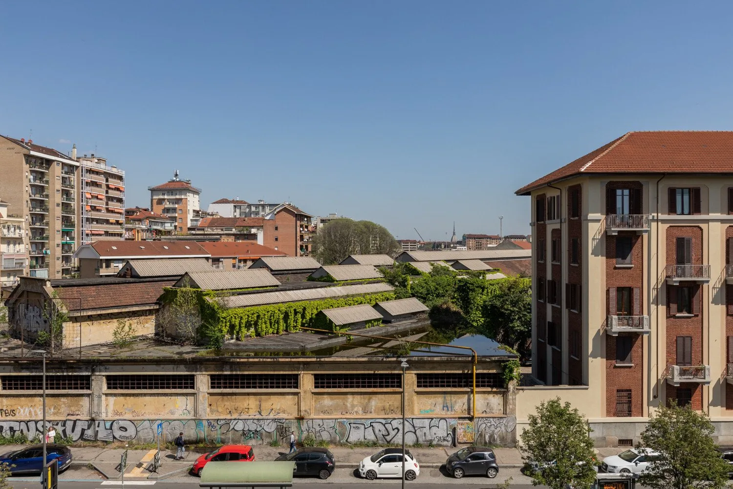 Un paisaje urbano de edificios residenciales, tejados y coches aparcados bajo un cielo despejado.
