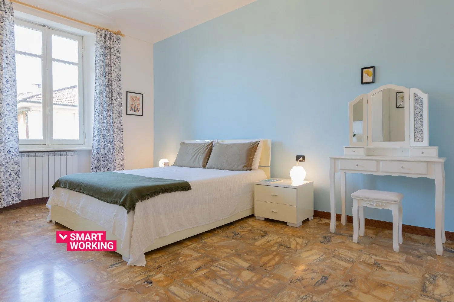 Un dormitorio con una cama, una mesita de noche y un tocador junto a una pared azul claro.