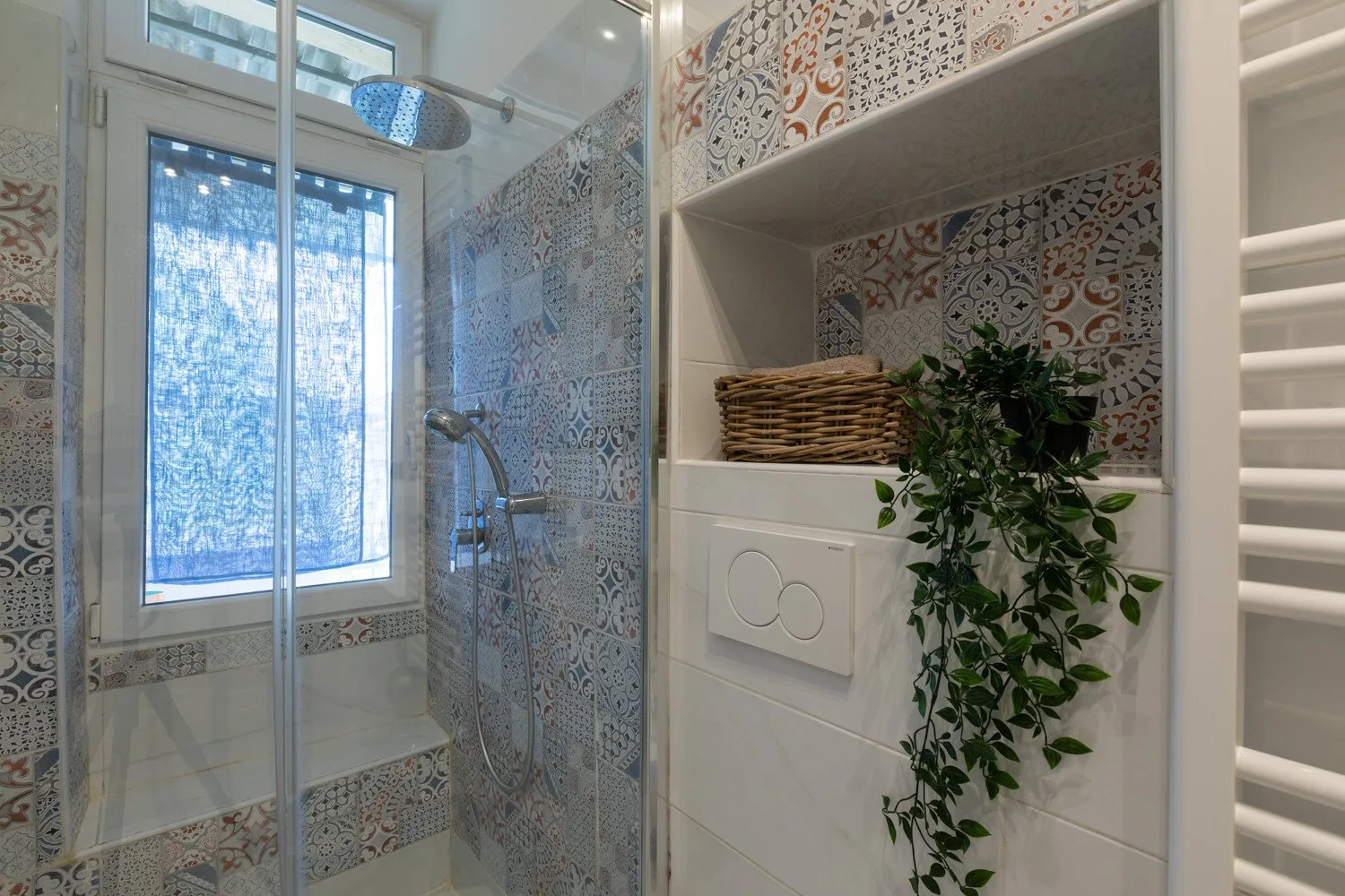 Un baño alicatado con una ducha de vidrio y un estante empotrado con una planta.