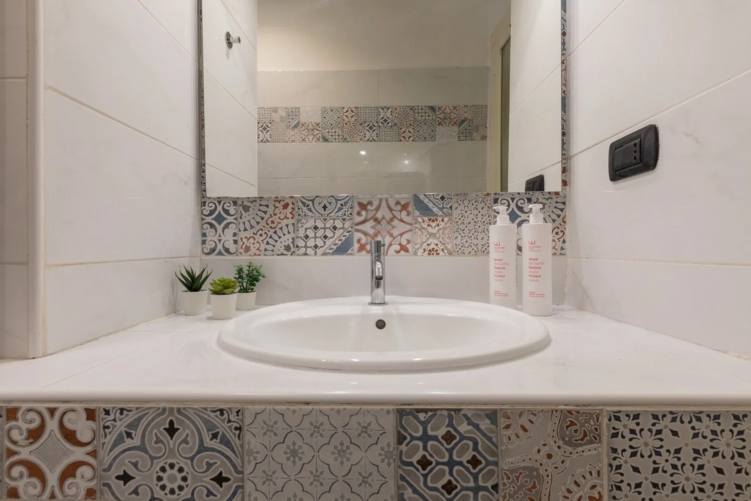 Un lavabo de baño alicatado con espejo y pequeñas plantas en macetas.