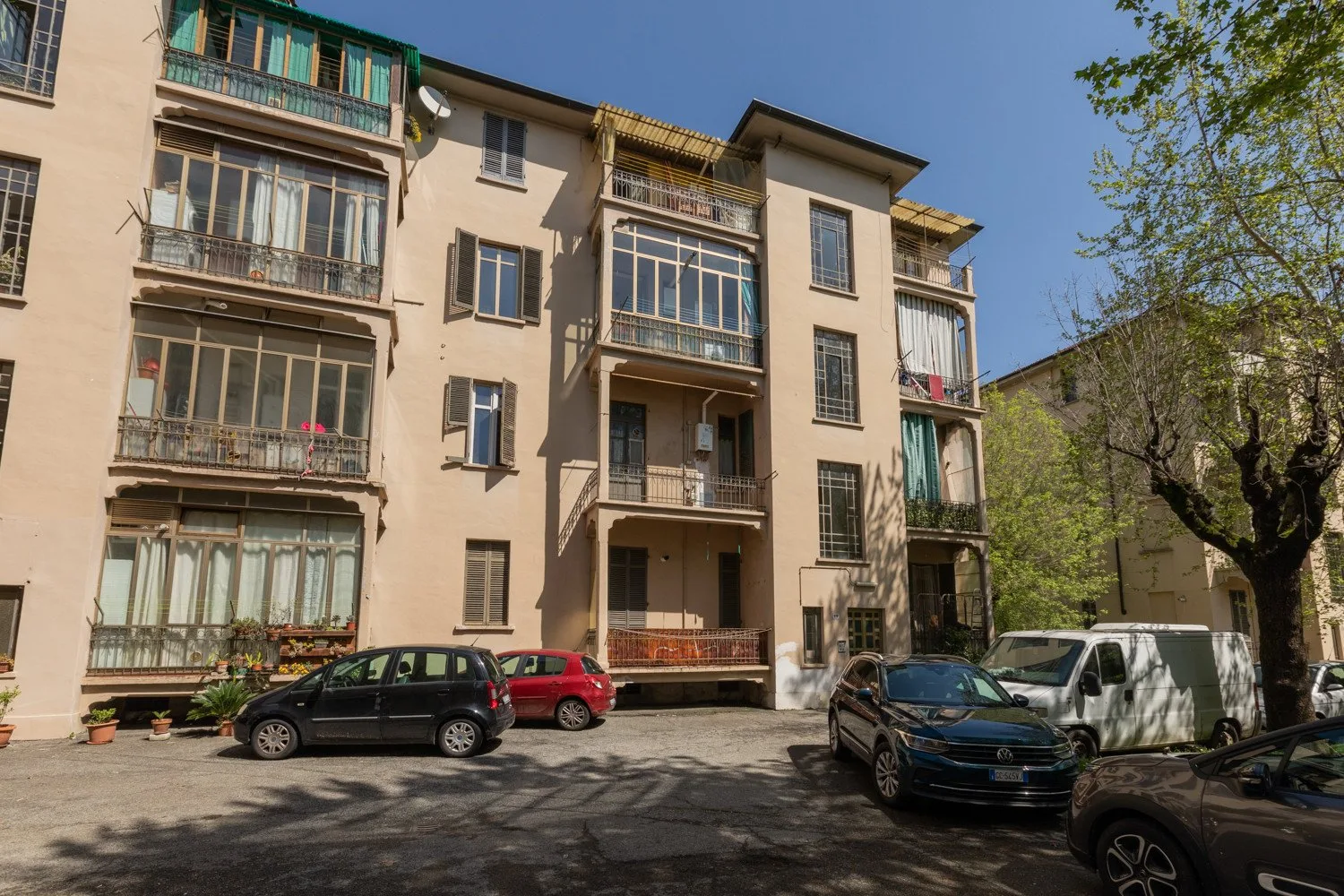 Un edificio de apartamentos de varias plantas con balcones da a una calle arbolada con coches estacionados.