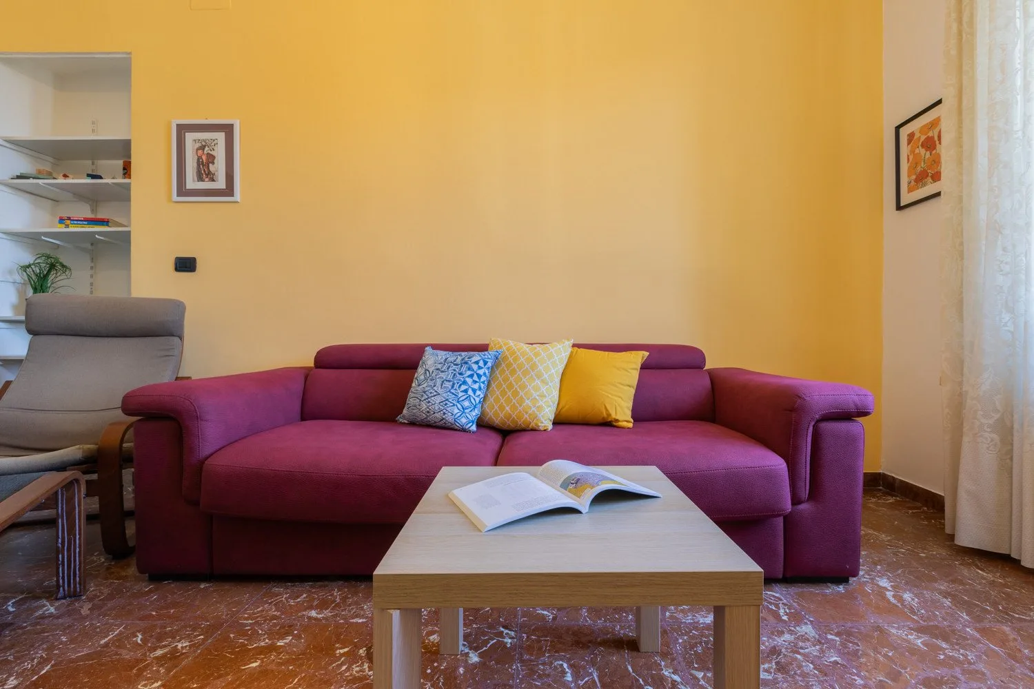 Una sala de estar con un sofá morado y un libro abierto sobre la mesa de centro.