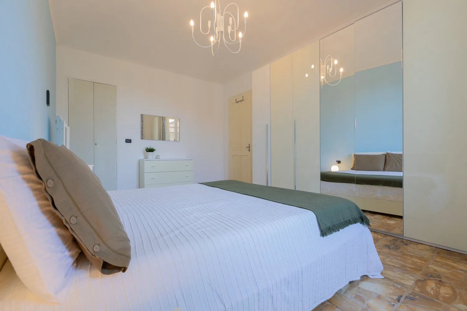 Un dormitorio con una cama bien tendida y puertas de armario con espejo.