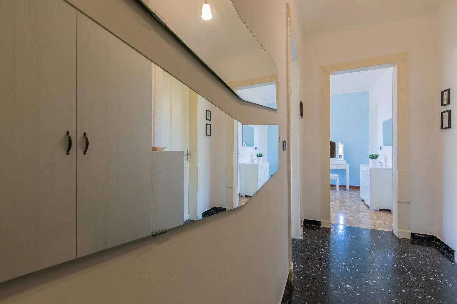Un pasillo con un espejo grande y una puerta abierta a una habitación luminosa.