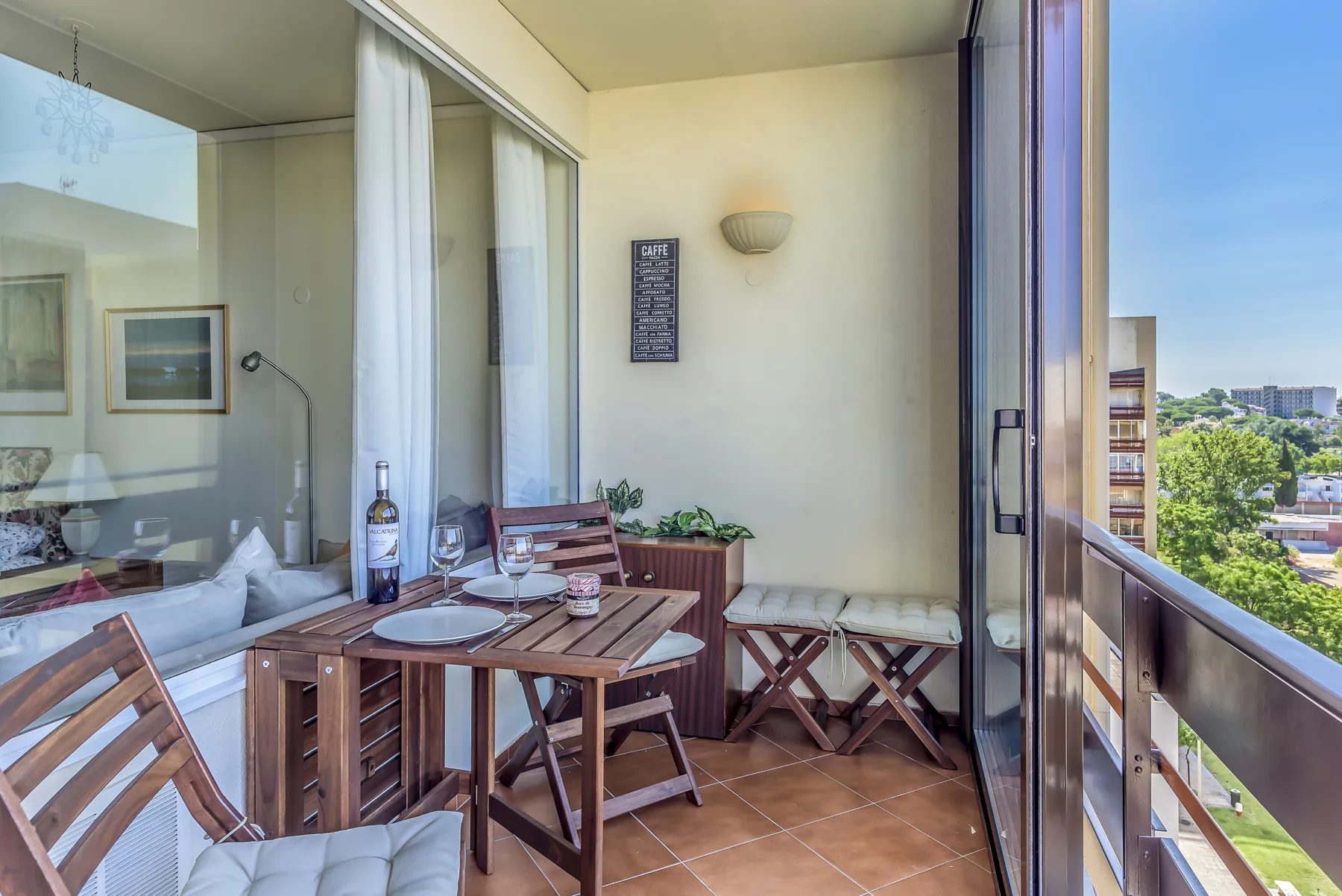 A balcony dining area with a wooden table and chairs beside glass doors.
