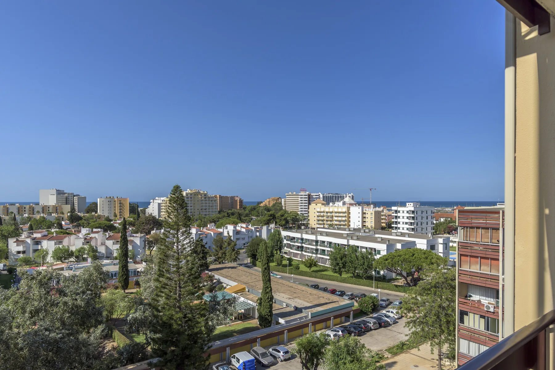 Vista de una ciudad costera con edificios de apartamentos, árboles y el mar al fondo.