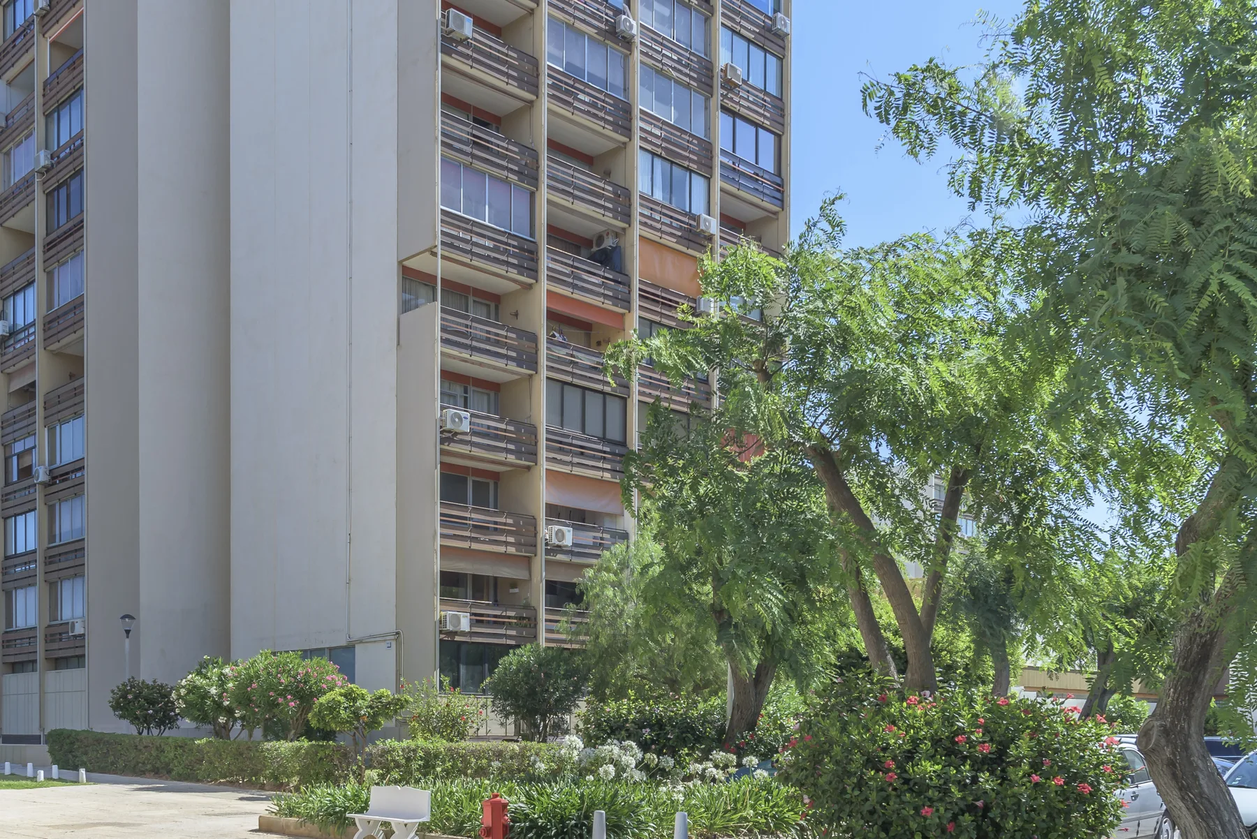 Exterior de un edificio de apartamentos con balcones, árboles y jardines.