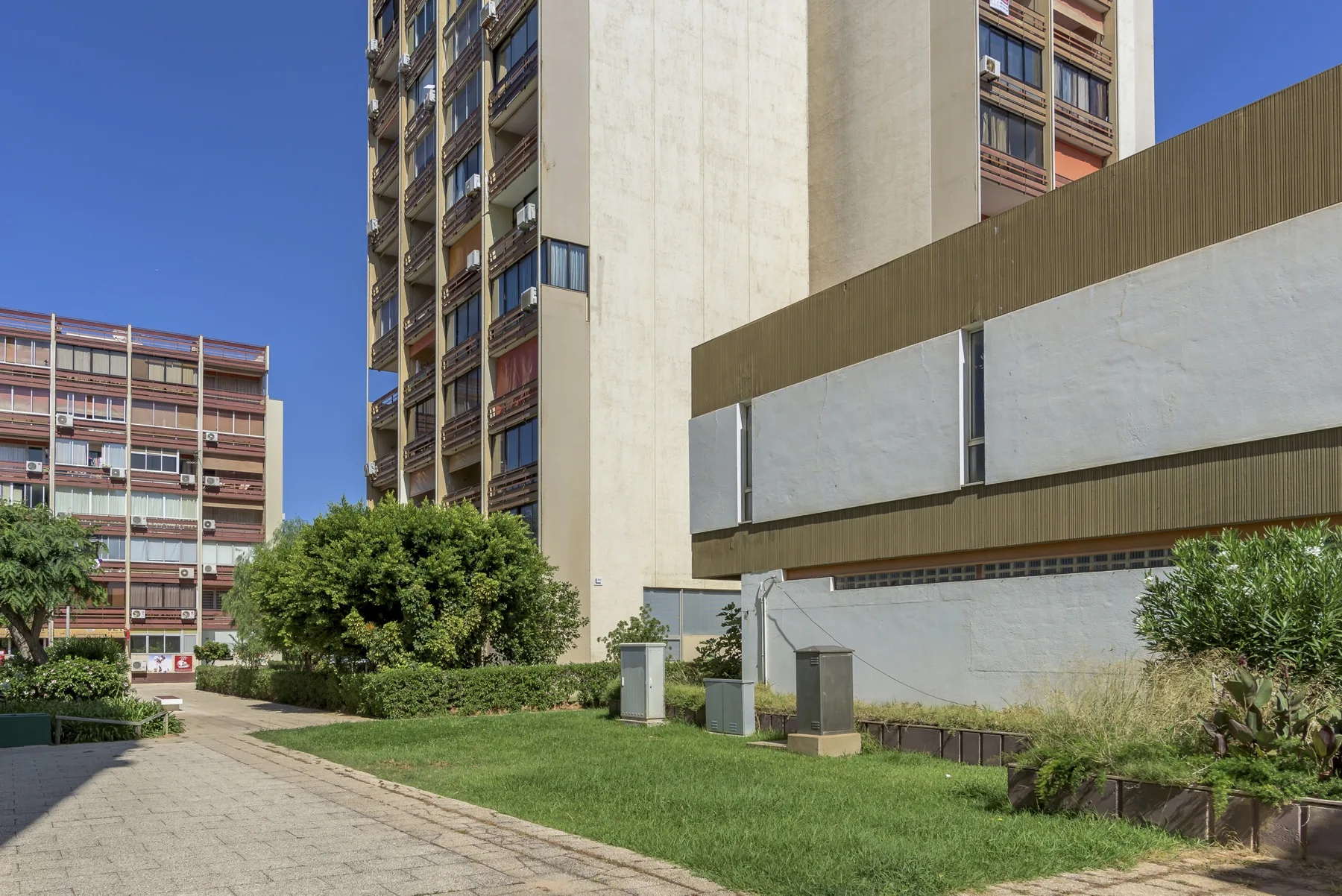 Un sendero pavimentado bordea una zona ajardinada y edificios de apartamentos modernos.