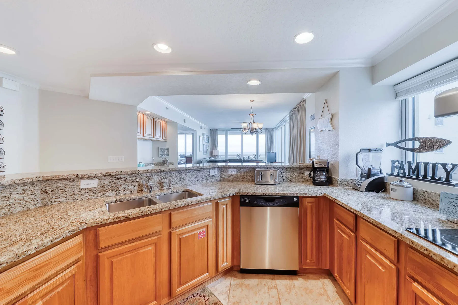 Una cocina luminosa tiene gabinetes de madera, encimeras de piedra y un lavavajillas de acero inoxidable.
