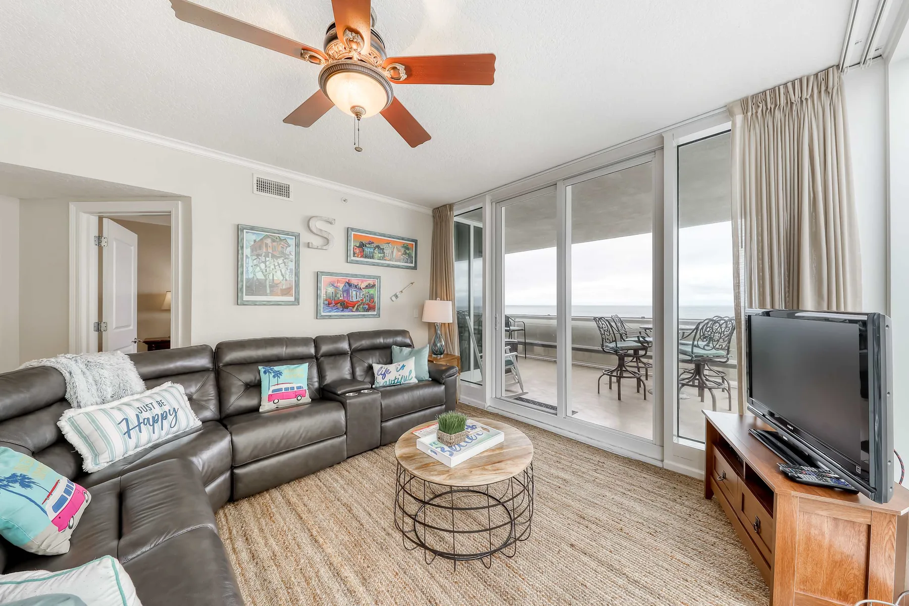 A living room with sectional seating, a coffee table, and sliding glass doors opening to a balcony.