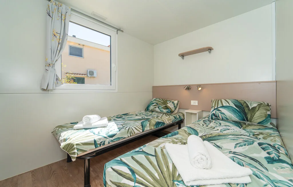 Un dormitorio con dos camas vestidas con ropa de cama estampada con hojas verdes.
