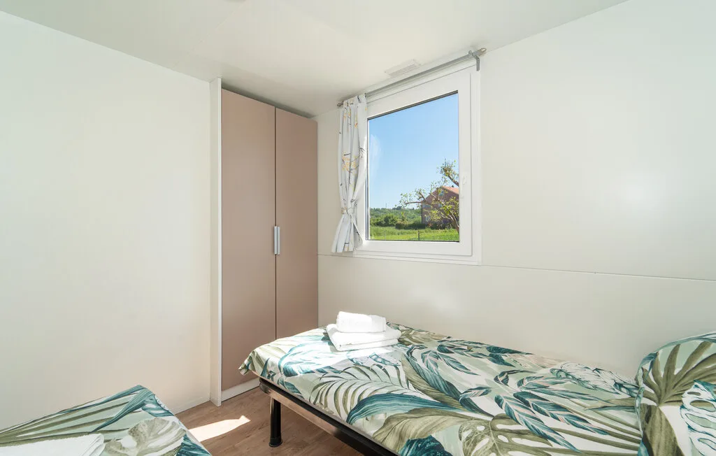 Un dormitorio con camas cubiertas de ropa de cama verde con hojas, junto a una ventana.