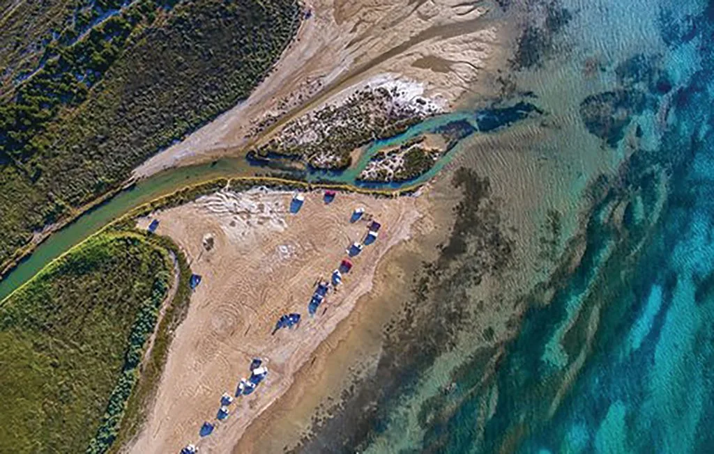 Vista aérea de una costa arenosa donde un arroyo estrecho desemboca en el mar.