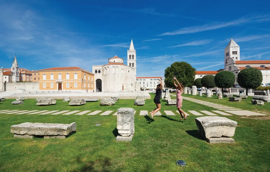 Un cementerio histórico con césped, tumbas de piedra y edificios religiosos claros al fondo.