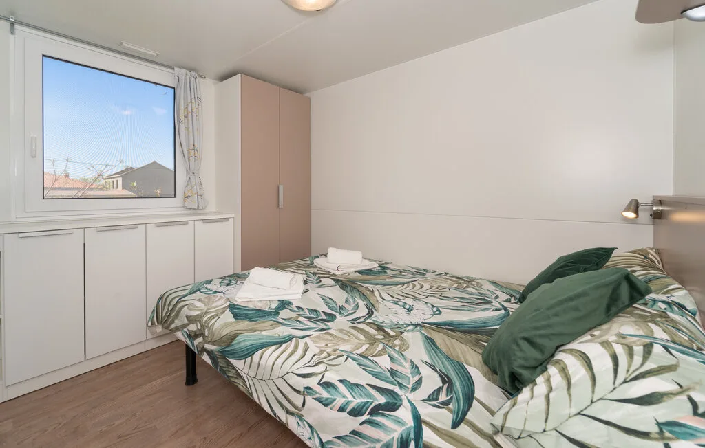 Un dormitorio con una cama cubierta con ropa de cama de hojas junto a una ventana.