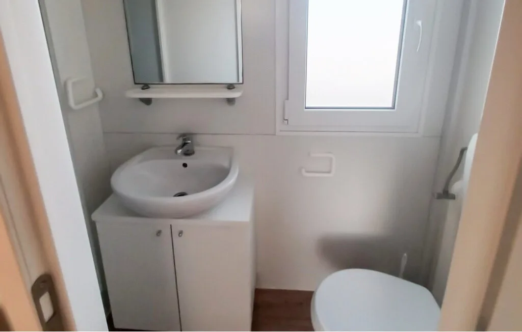 Un baño pequeño con lavabo, espejo, ventana e inodoro.