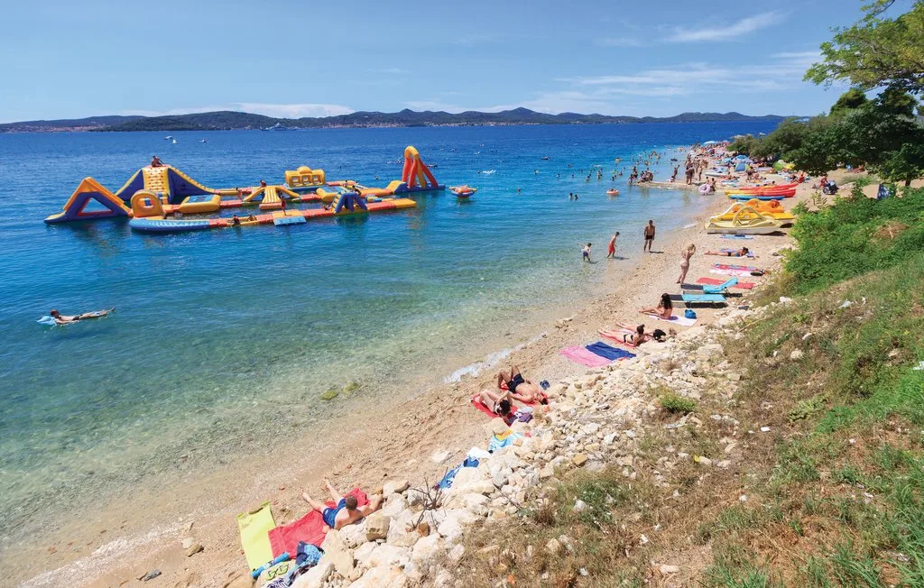 Una playa concurrida con bañistas y un parque acuático inflable mar adentro.