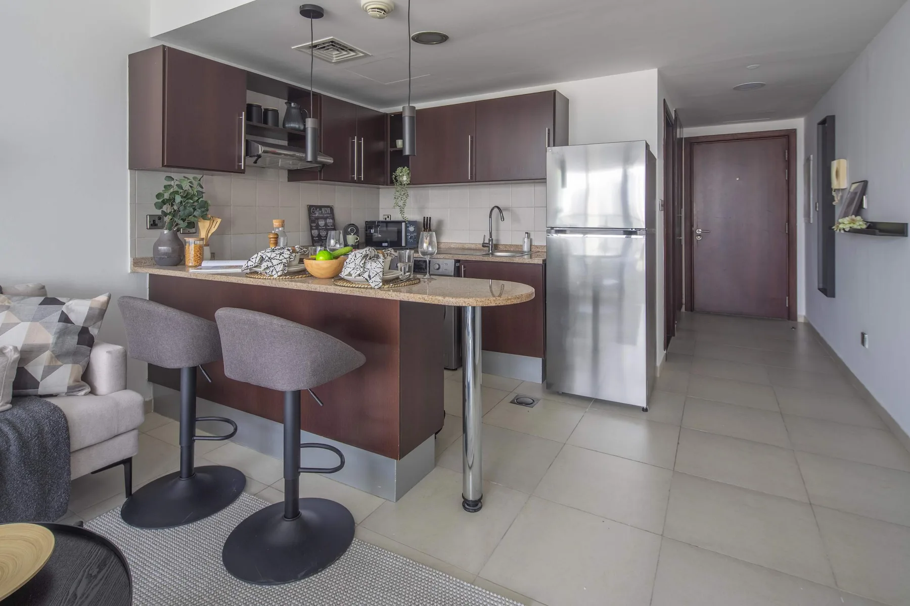 A modern kitchen with a counter and bar stools opens onto a small seating area.