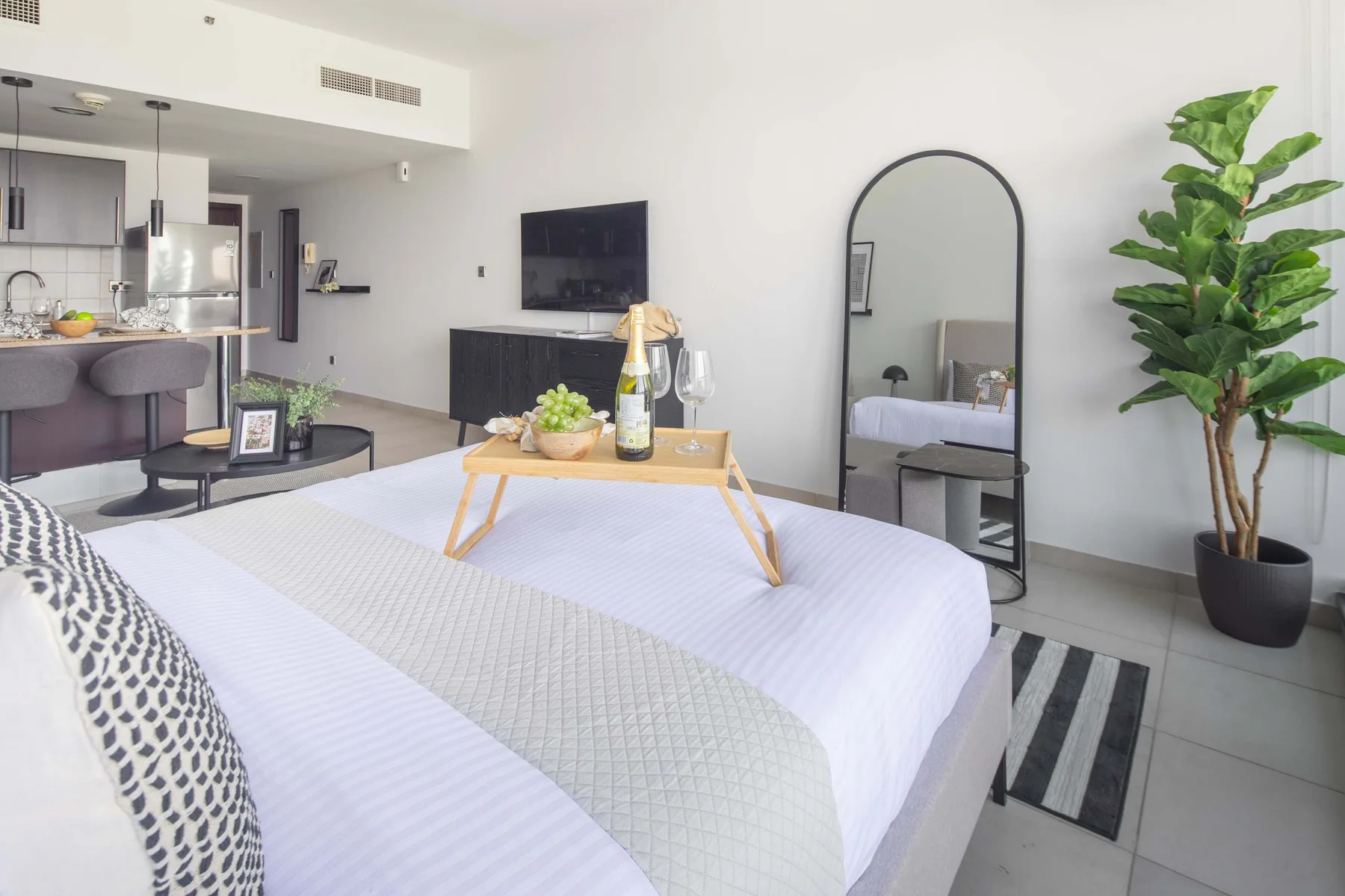 A bedroom with a neatly made bed, an arched mirror, and a potted plant.