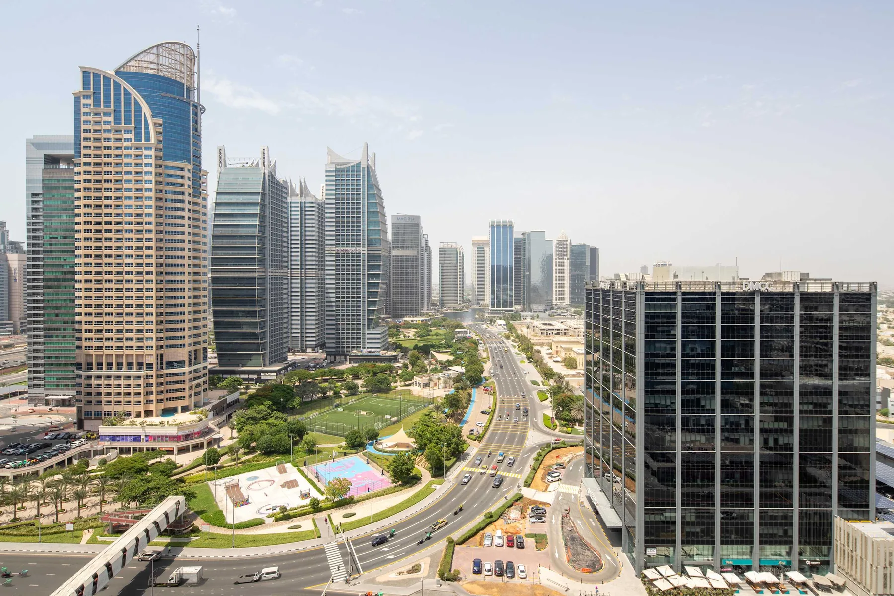 A city skyline overlooks a curving road and landscaped green spaces.