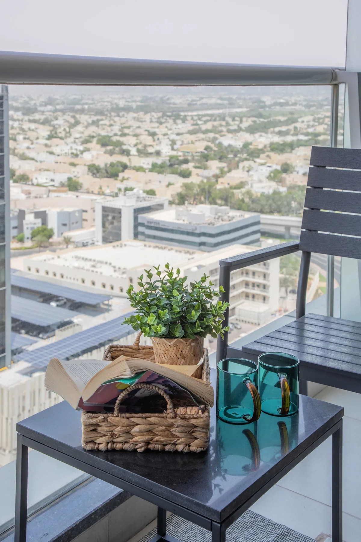 A balcony seating area with a table, woven basket, and city view through glass.
