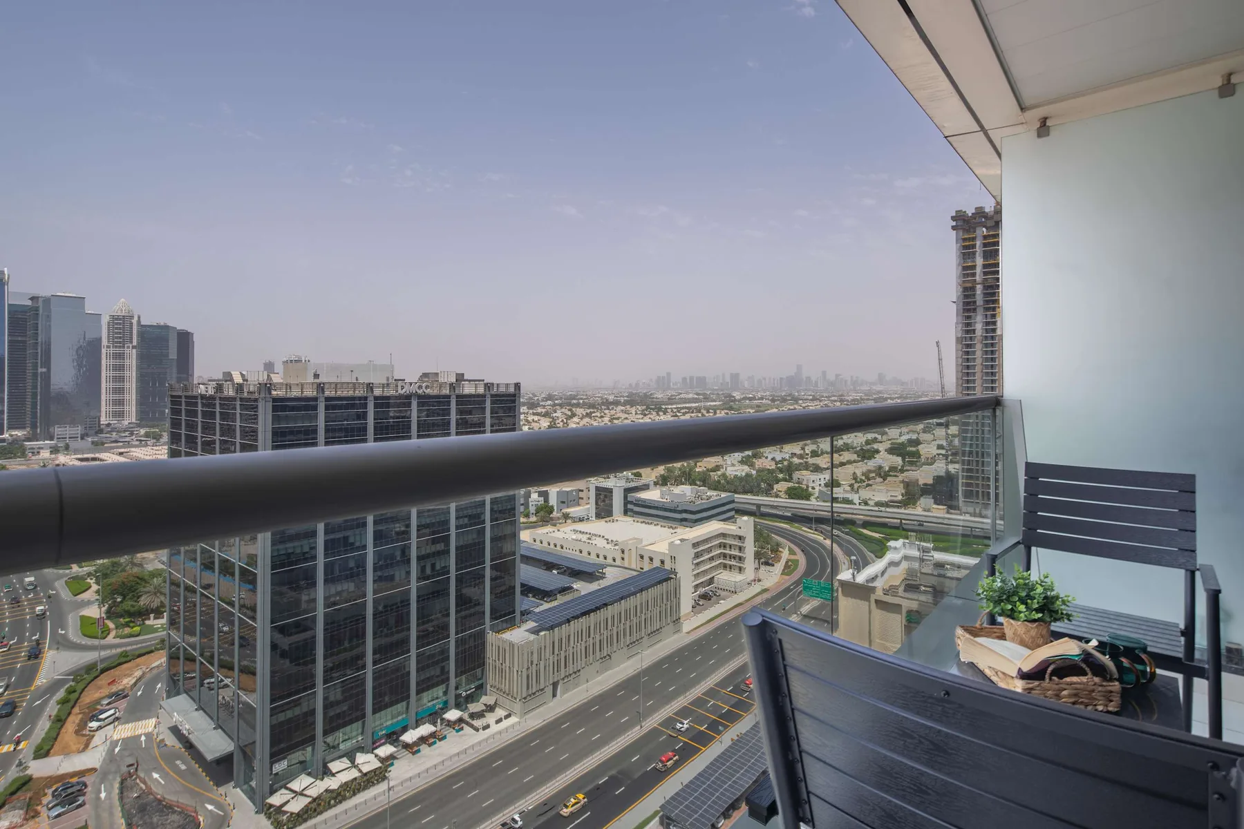 A balcony overlooks city buildings and roads, with outdoor seating beside the railing.
