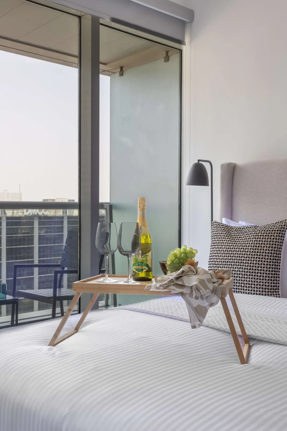 A bedroom with a low table set across the bed beside floor-to-ceiling windows.