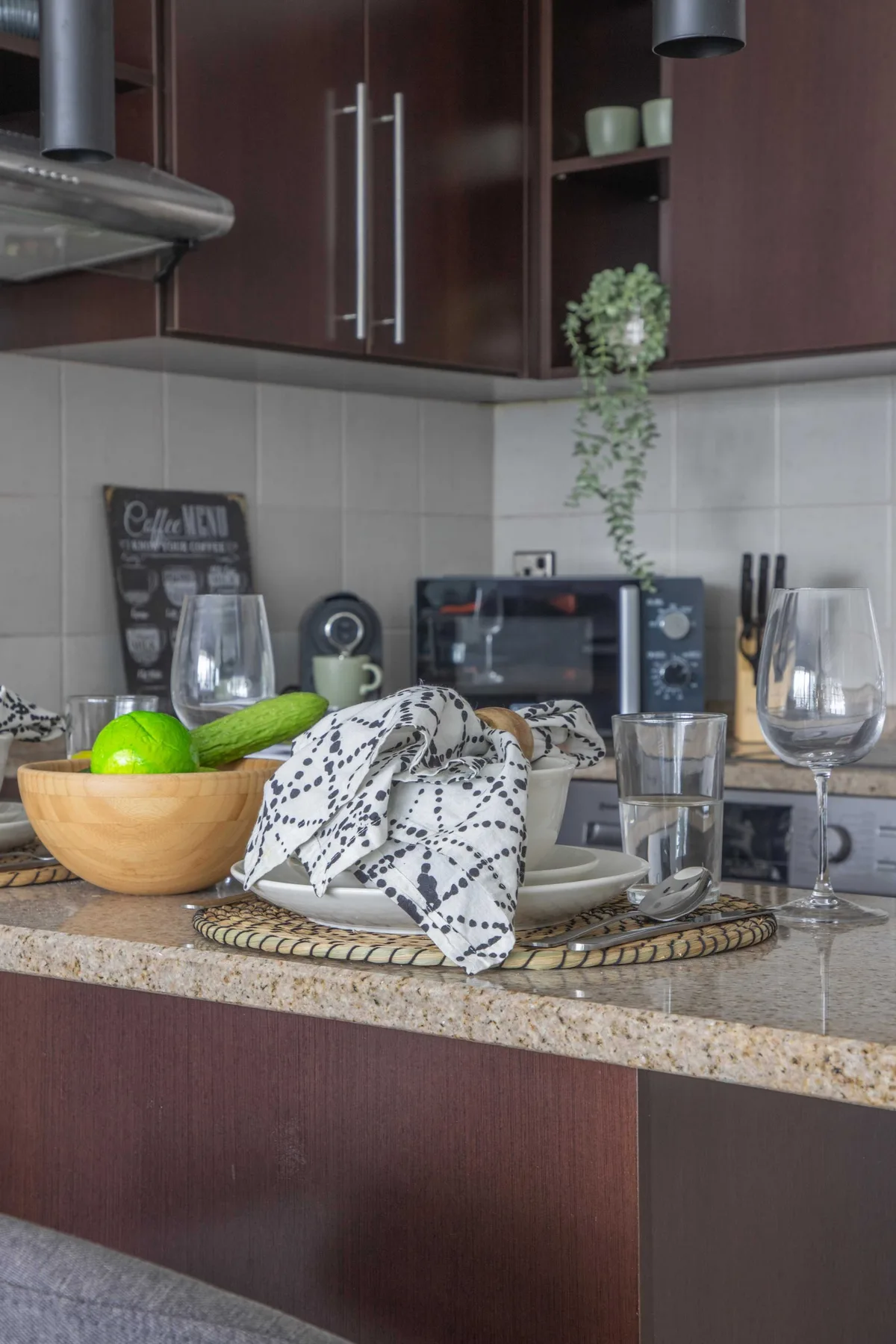 A kitchen counter with fruit, glasses, dishes, and dark wood cabinets.