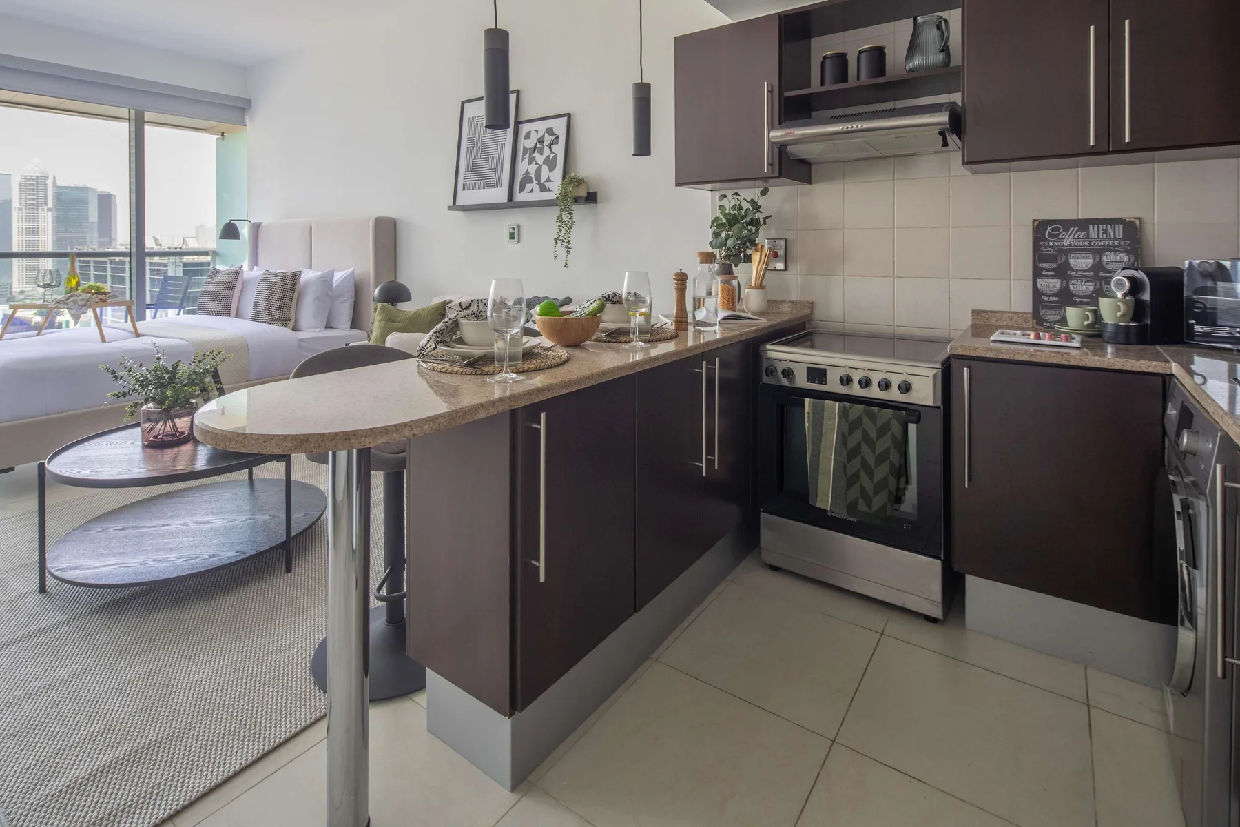 A modern kitchen with a breakfast counter, beside a living area with large windows.