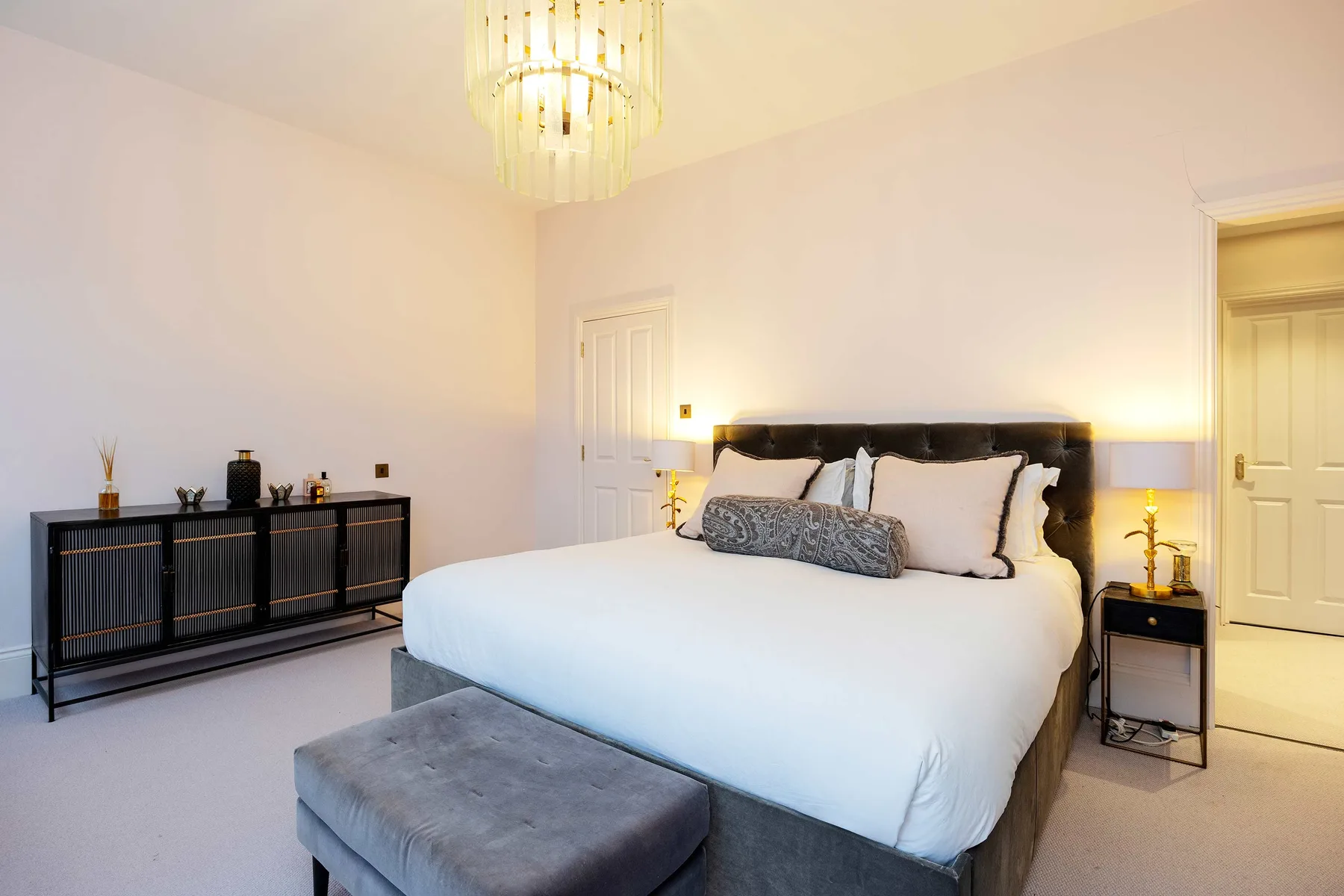 A bright bedroom with a large bed, bedside tables, and a chandelier.