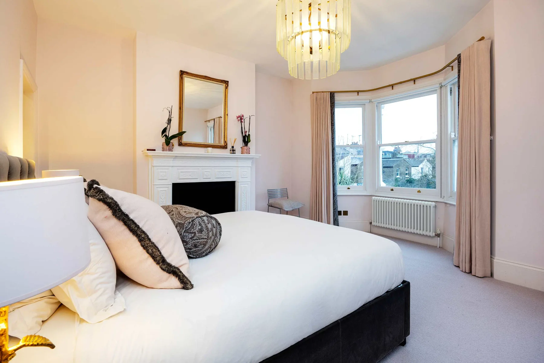 A bright bedroom with a large bed, fireplace, and bay window.
