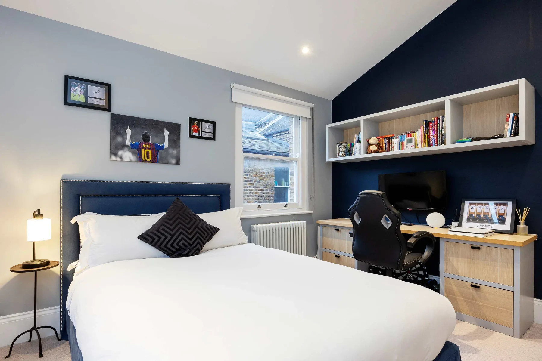 A bedroom with a bed and a desk against a dark blue wall.