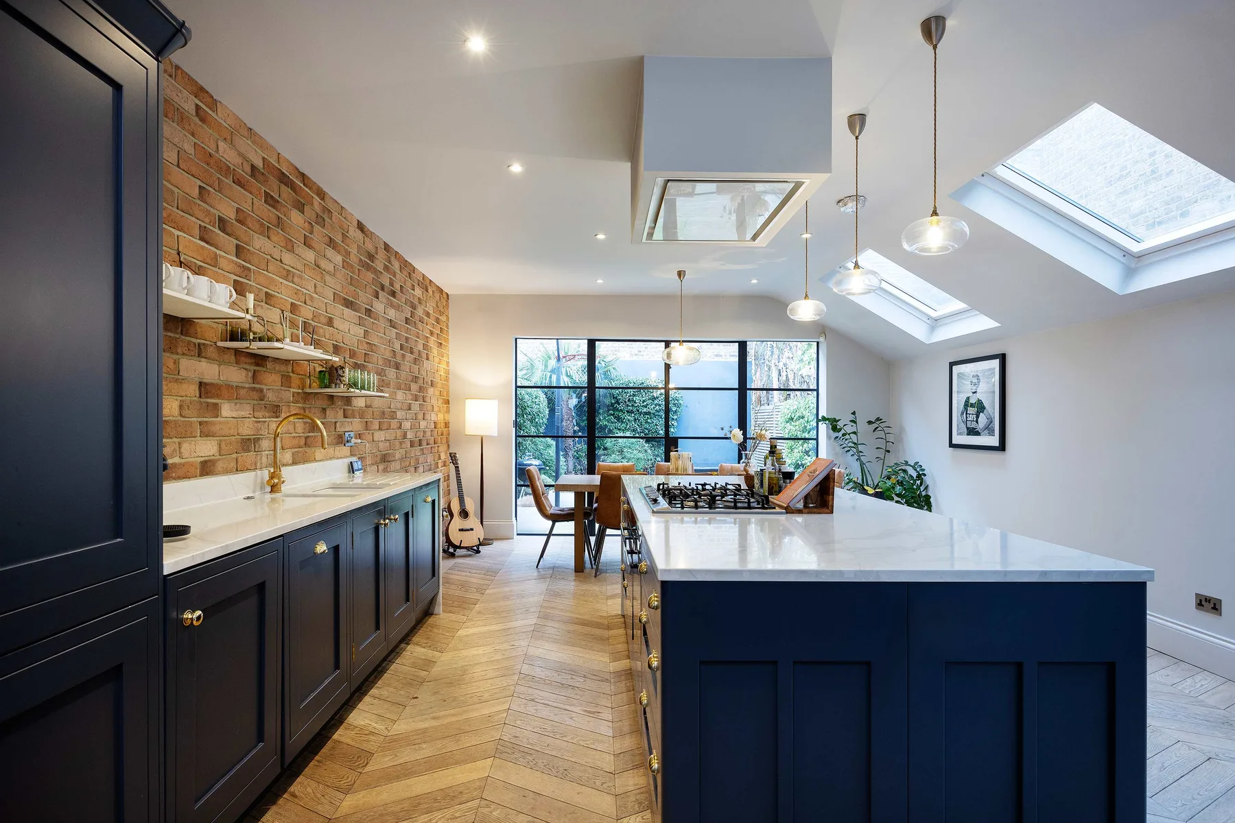 A bright kitchen with a large island, brick wall, and skylights.
