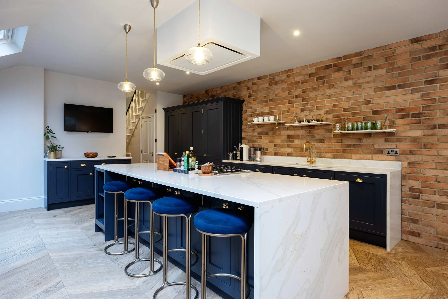 A bright kitchen with a large island, dark cabinetry, and exposed brick walls.