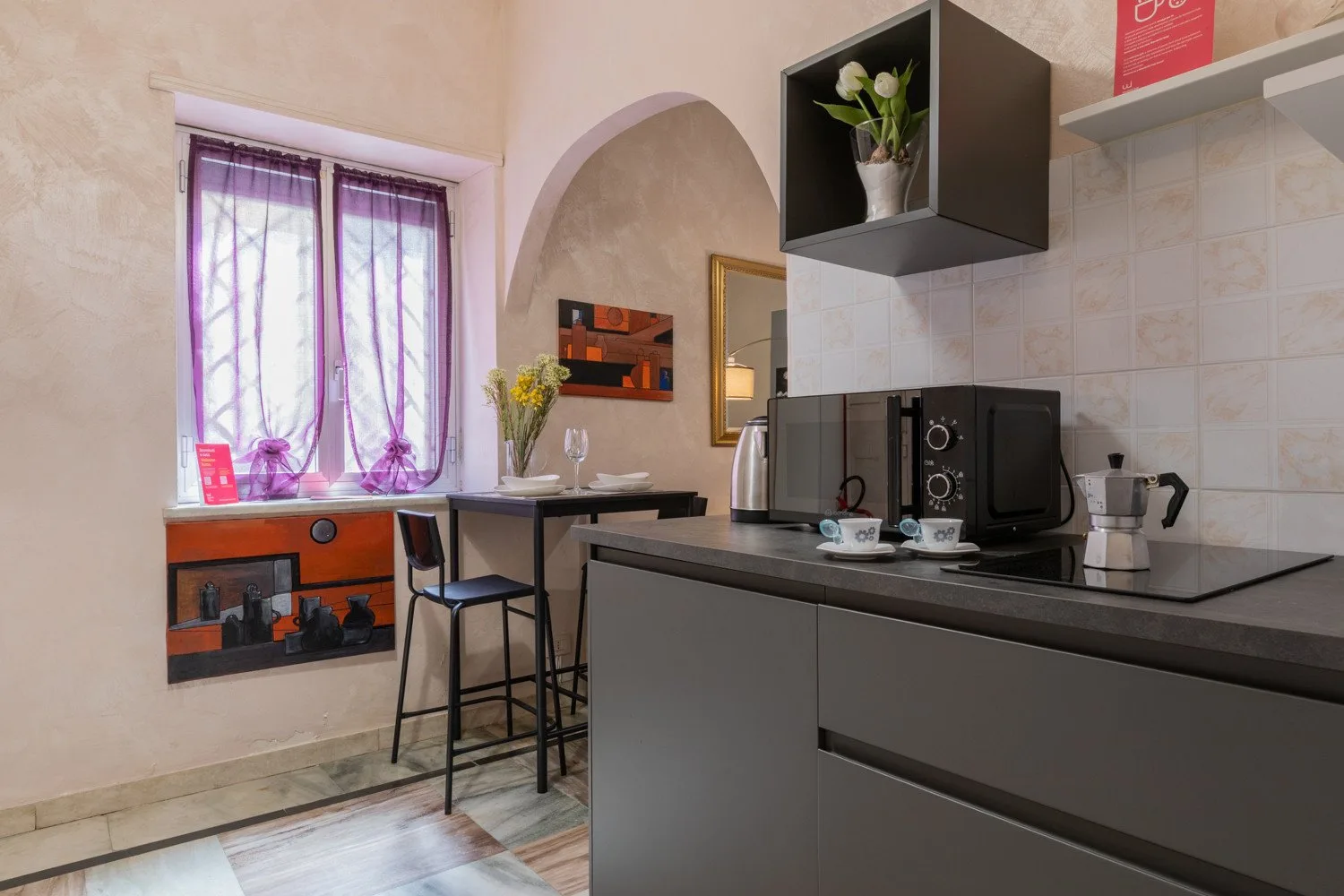 Una cocina con una encimera, pequeños electrodomésticos y una ventana con cortinas moradas.