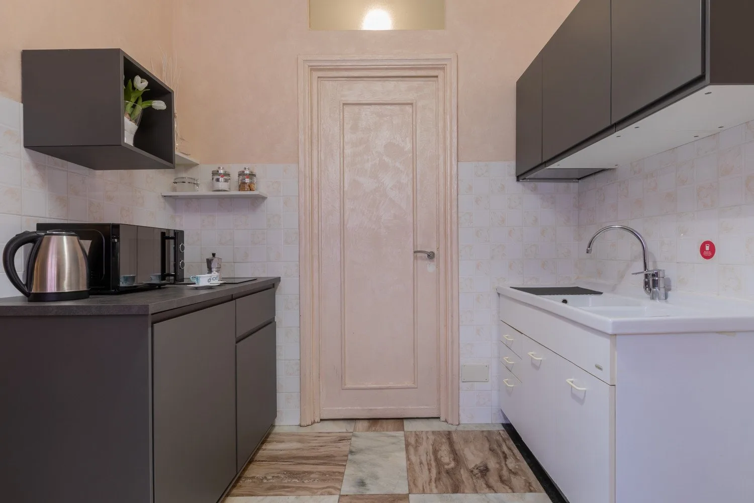 Una cocina compacta con gabinetes oscuros, encimeras blancas y una puerta al centro.