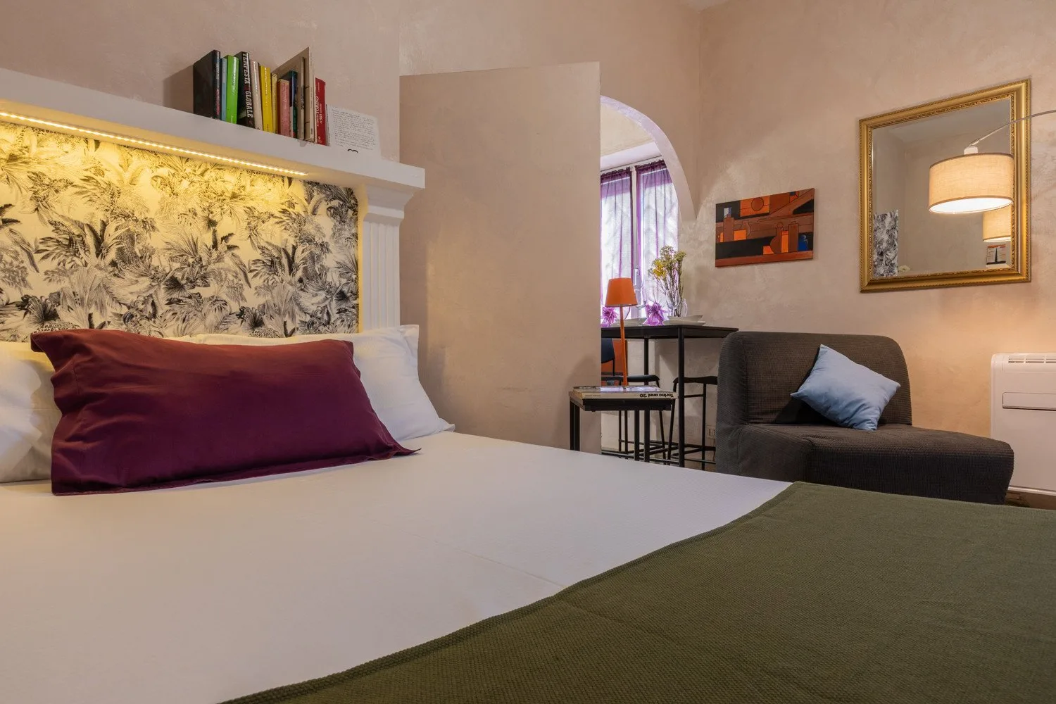 Un dormitorio con una cama y una pequeña zona de estar junto a una ventana arqueada.