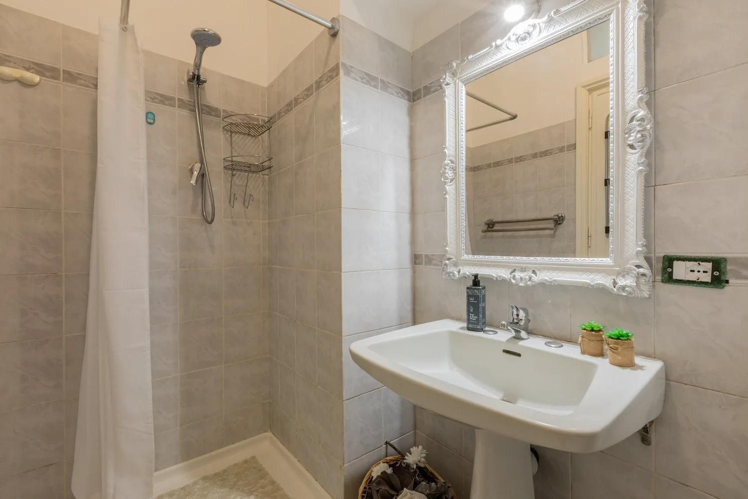 Un baño con azulejos, una ducha y un lavabo bajo un espejo enmarcado.