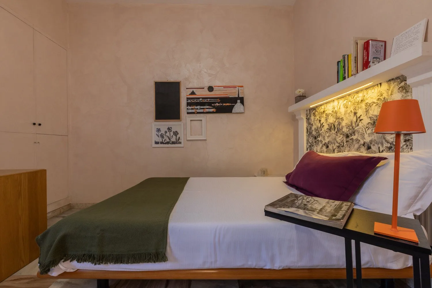 Un dormitorio con una cama tendida, almohadas moradas y una lámpara de noche.