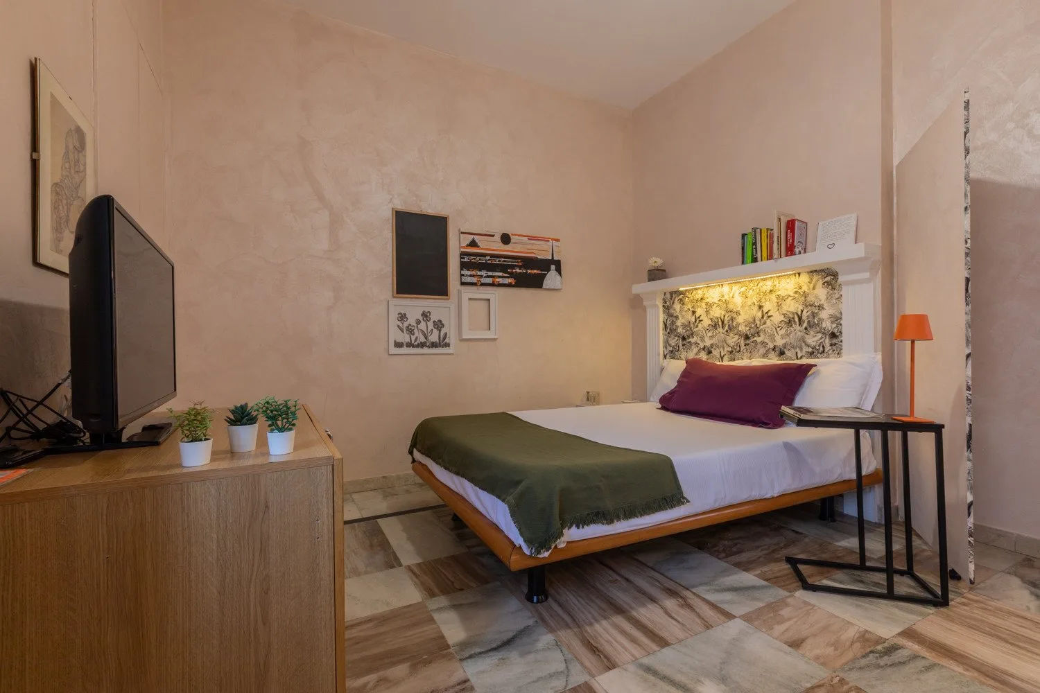Un dormitorio con una cama, un televisor sobre un mueble y una mesita auxiliar.