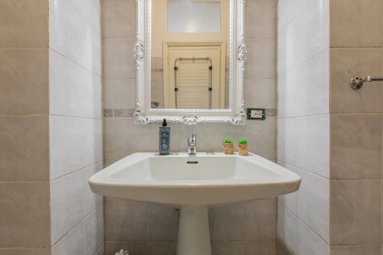 Un baño con azulejos, un lavabo con pedestal y un espejo enmarcado.