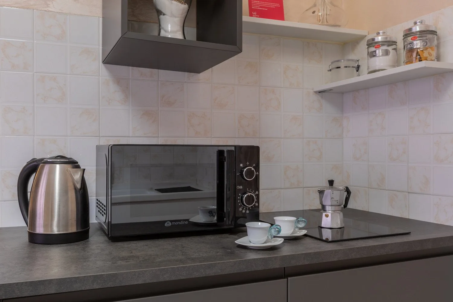 Una encimera de cocina alicatada tiene un microondas, un hervidor y una cafetera.