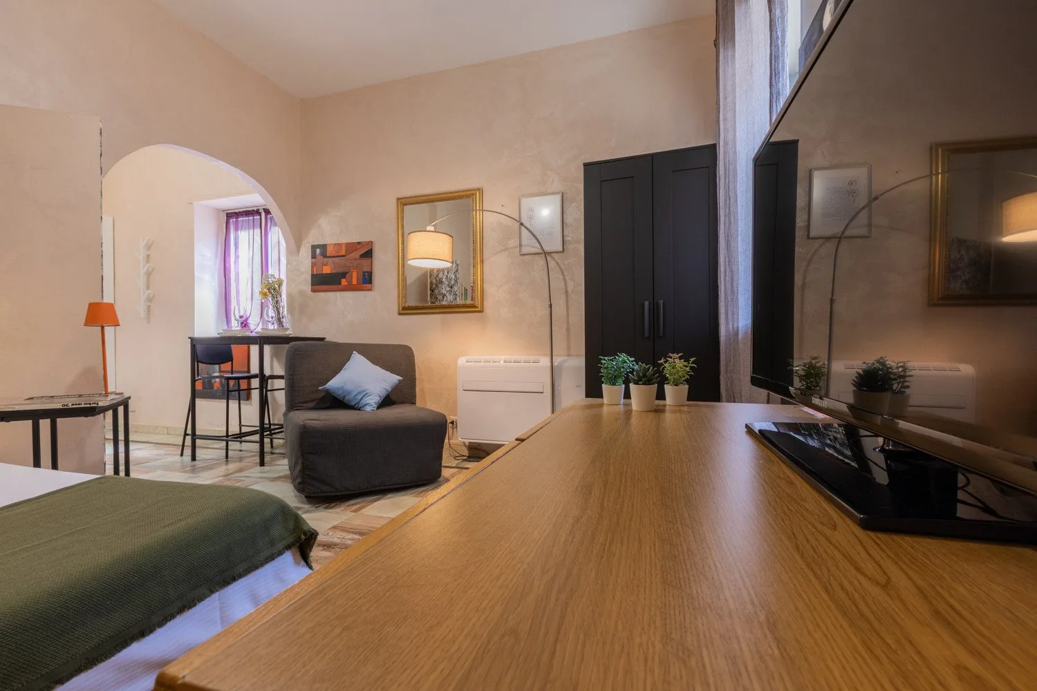 Dormitorio con zona de estar, escritorio, sillón y televisor.