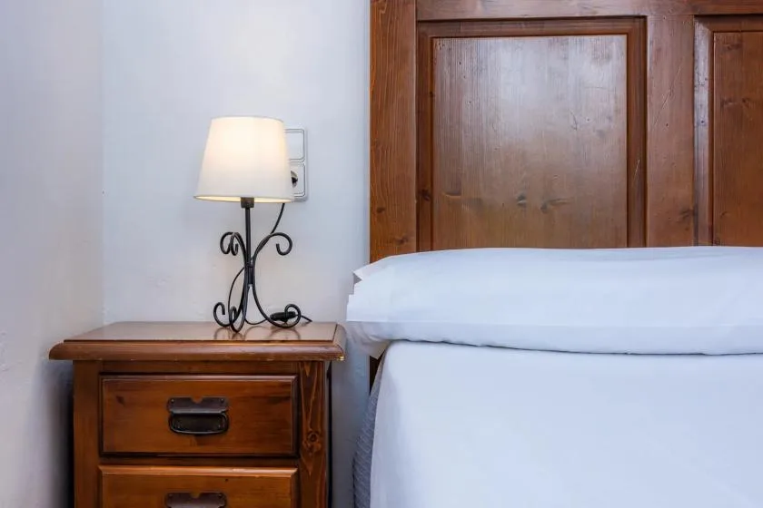 Un dormitorio con una cama tendida junto a una mesita de madera y una lámpara.
